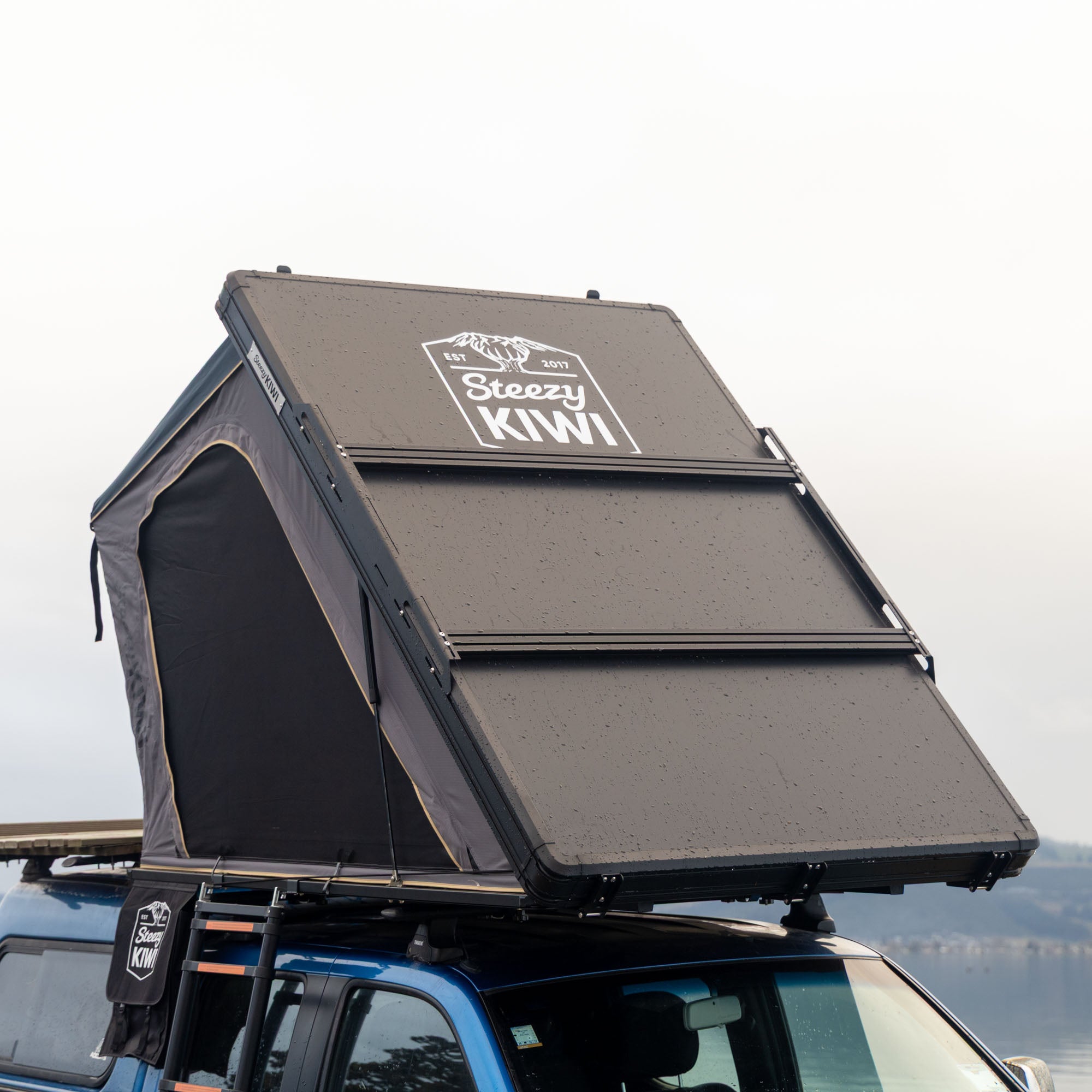 Roof top tent on a vehicle with 'Steezy Kiwi' branding against a clear sky.