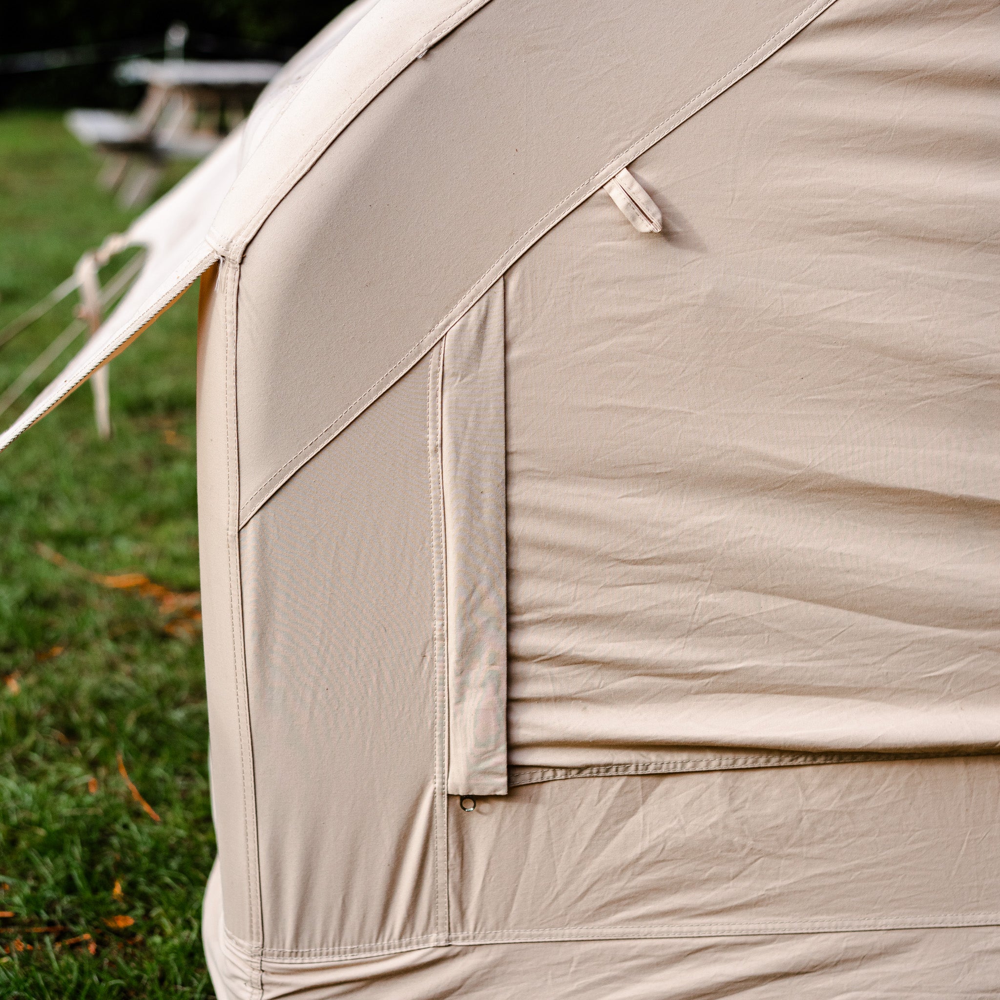 Close-up of a beige tent with grass and picnic table in the background